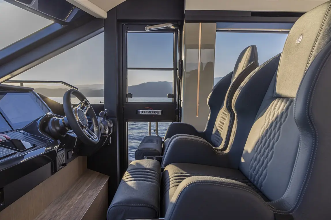 Interior view of a luxury boat cockpit featuring a steering wheel, advanced controls, and comfortable seating with lake scenery.
